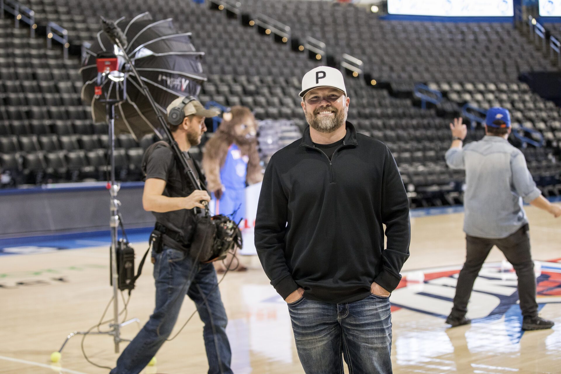 person wearing a black sweater and baseball cap stands inside a sports arena